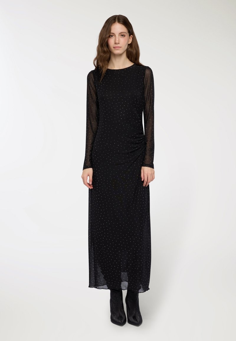 Czarna sukienka z długim rękawem z przezroczystą nakładką, z małymi srebrnymi kropeczkami i marszczonym detalem z boku. Stylizowana z czarnymi botkami za kostkę.