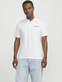 Valkoinen polo paita, jossa on kaulus ja musta "JACK & JONES" -logo vasemmalla rinnalla. Yhdistetty vaaleansinnihin farkkuihin, jotka korostavat rentoa istuvuutta.