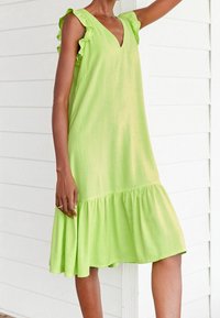Robe vert lime avec des manches à volants, décolleté en V et ourlet en étages. Fabriquée en tissu léger, elle possède une silhouette fluide et une texture douce.