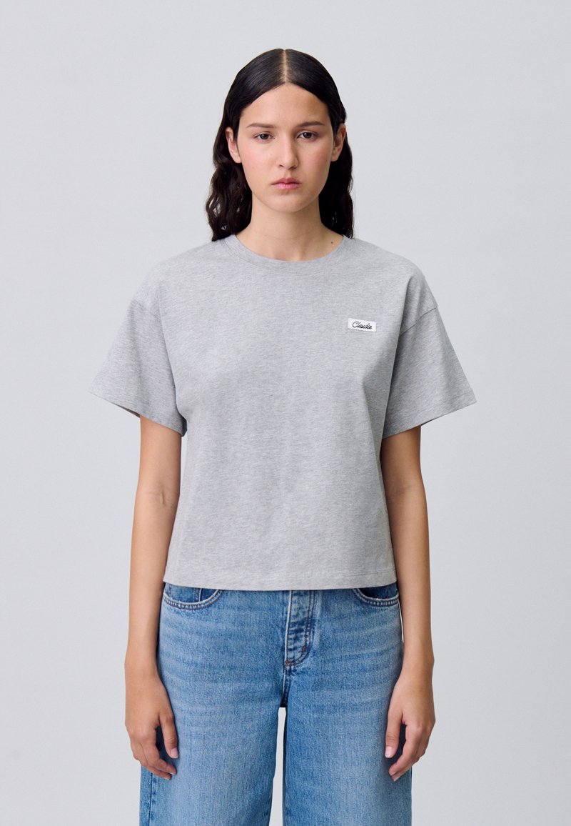 T-shirt grigia cropped in cotone, con maniche corte e collo rotondo. Un piccolo etichetta bianca con testo nero è cucita sul davanti.