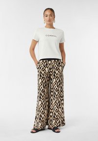 Weißes T-Shirt mit kurzen Ärmeln und dem Text "COMMA," kombiniert mit weiten, gemusterten Hosen mit abstraktem Schwarz- und Beigedesign.