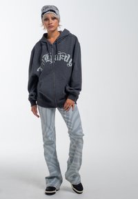 Sudadera gris con cremallera y gran texto blanco, combinada con jeans acampanados de color azul claro con un patrón de cebra. Zapatillas negras con acentos blancos.