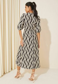 Rochie cu un model de valuri alb-negru, cu mâneci bufante și talie strânsă, având o fustă fluidă. Modelul poartă sandale cu toc nude cu barete.