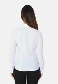 Camicia bianca a maniche lunghe con vestibilità su misura, colletto a punta e polsini con bottone. Tessuto liscio con dettagli sulle cuciture laterali.