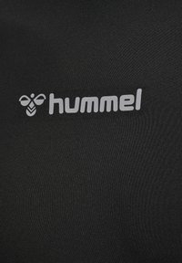 Czarna koszulka sportowa o gładkiej fakturze, z wyraźnym szarym logo "hummel" oraz grafiką pszczoły nad logo.