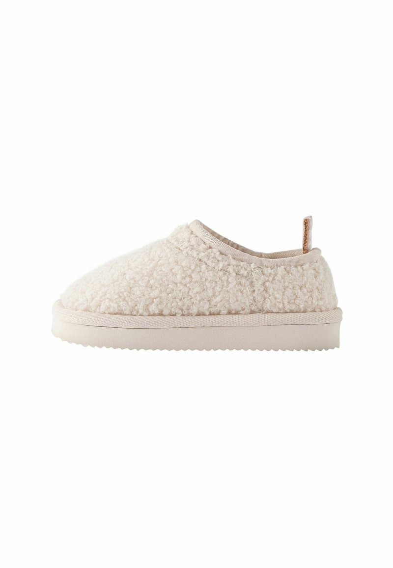 Chaussure beige clair sans lacets avec dessus texturé duveteux et semelle plate, équipée d'une petite languette en tissu au talon pour un enfilage facile.