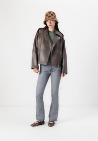 Brun lær bikerjakke med glidelåslommer, kombinert med en grønnstripet skjorte og lysegrå utsvingte jeans. Tilbehør er en mønstret bøttehatt.