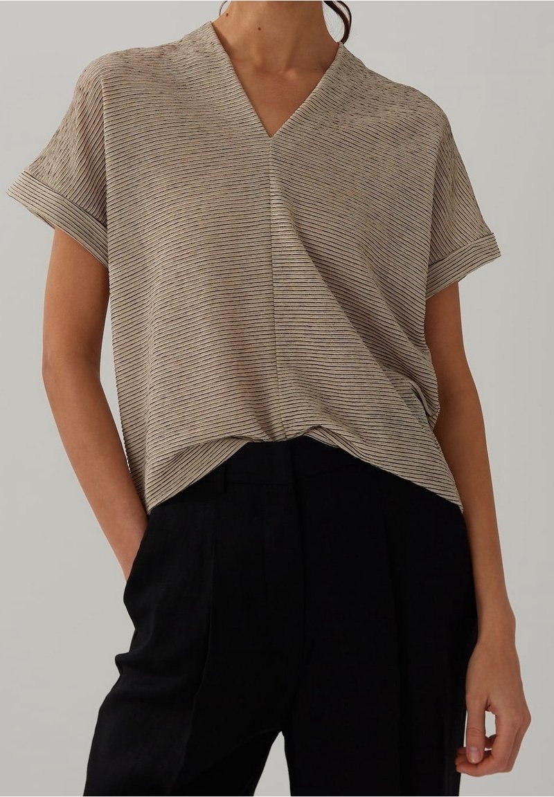 Volnější béžový top s vertikálními pruhy, V-výstřihem, krátkými ohrnutými rukávy a měkkou texturou, kombinovaný s černými kalhotami s vysokým pasem.