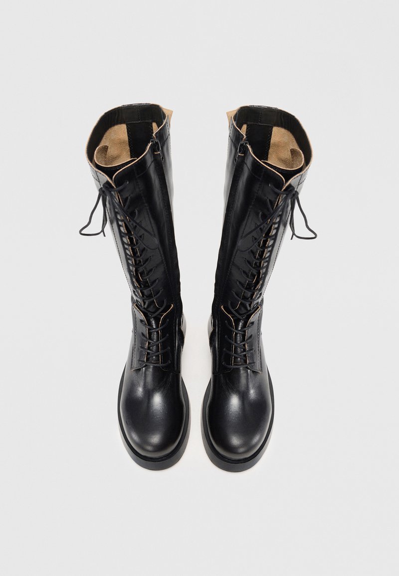 Black leather knee-high boots feature a lace-up front and inner zipper. Smooth texture with a tan lining and flat rubber sole.