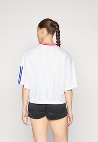 Witte korte mouwen shirt met een ronde rode kraag, voorzien van blauwe strepen op de mouwen. Gecombineerd met zwarte shorts.