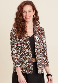 Patroon blazer in crème, zwart en roest met bloemenontwerp, sluiting met één knop en ritszakdetail. Kruidige haren en oorringen.
