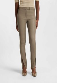 Slim-fit, olive green leather pants with side slits at the ankles, featuring a subtle sheen and front zip closure. Smooth texture.