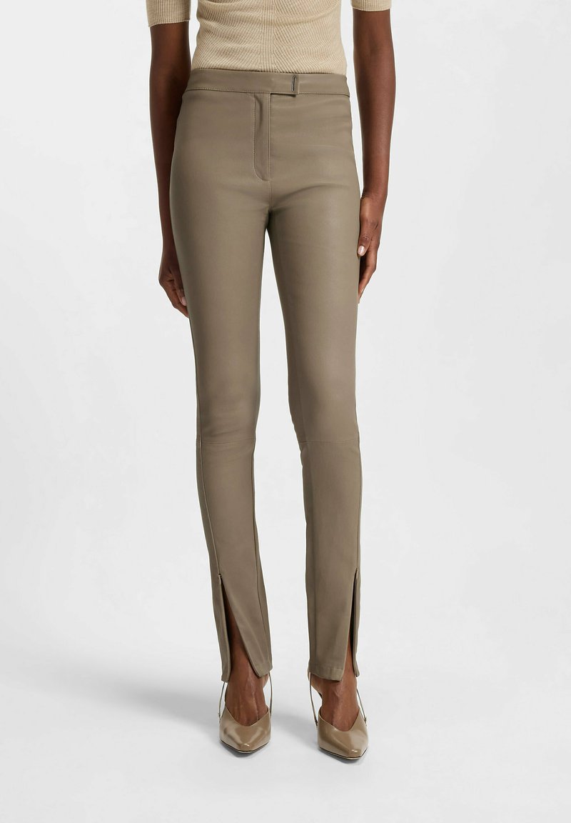Slim-fit, olive green leather pants with side slits at the ankles, featuring a subtle sheen and front zip closure. Smooth texture.