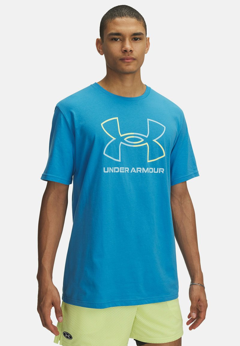 Camiseta de algodón azul con logo en perfil amarillo y manga corta. Cuello redondo y corte recto, llevada sobre pantalones cortos de malla verde claro.