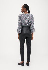 Calças de couro pretas de cintura alta combinadas com uma blusa de padrão floral com mangas amplas. Sapatilhas pretas minimalistas complementam o visual.