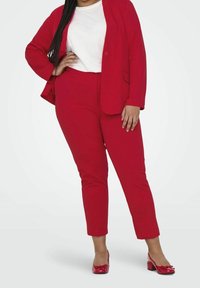 Röd skräddarsydd blazer och matchande tapered-byxor, tillsammans med en vit skjorta. Lystna röda klackar ger en elegant fulländning till outfiten.