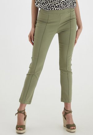 Olijfgroene, getailleerde broek met een gladde textuur, voorzien van decoratieve stiksels en een verkorte lengte, gecombineerd met tan espadrille hakken.