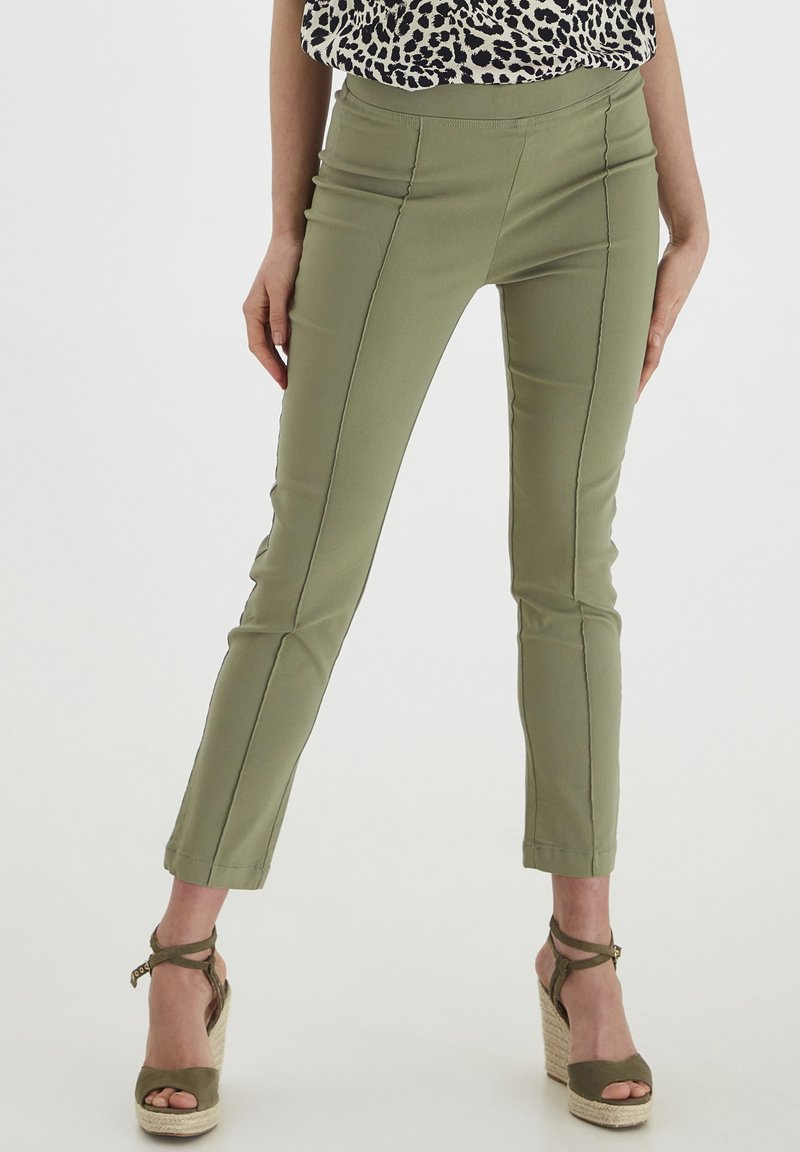 Pantalons ajustés vert olive avec une texture lisse, dotés de coutures décoratives et d'une longueur cropped, associés à des talons espadrilles beige.