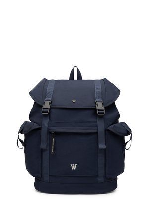 Mochila azul marino con tapa abatible, dos correas frontales con hebilla, bolsillo frontal con cremallera, bolsillos laterales y un asa superior en forma de anilla.