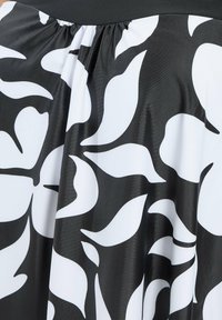 Tissu noir et blanc avec de grands motifs abstraits de feuilles audacieux et un détail froncé près du bord supérieur.