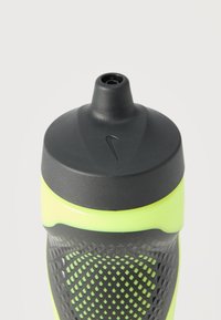 Κοντινή λήψη ενός μαύρου και νέον κίτρινου μπουκαλιού νερού Nike με υφή για καλύτερο κράτημα και καπάκι με στόμιο τύπου push-pull.