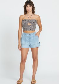 Abgeschnittenes, trägerloses Oberteil mit einem schwarz-weißen Palmenblattmuster und einem Schlüssel-Auschnitt, kombiniert mit hellblauen, hochgeschnittenen Jeans-Shorts.