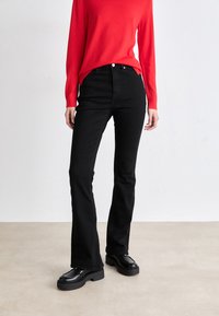 Vaqueros de campana negros con una textura suave, combinados con un suéter rojo ajustado. Los zapatos son gruesos y negros con un acabado pulido.