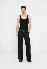 Débardeur noir à encolure dégagée associé à un pantalon noir côtelé à jambes larges et une ceinture noire avec boucle circulaire.