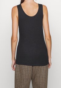 Svart ärmlös linne med rundad halsringning, tillverkat av mjukt jersey-tyg, som är kombinerat med mönstrade hundtandsbyxor.