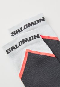 Juodos ir baltos sportinės kojinės su raudonais akcentais. Ant viršaus yra logotipas "SALOMON". Pagamintos iš tekstūrinio mezgimo medžiagos.