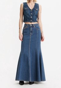 Denim dvoudílný outfit se skládá z bezrukávového cropped topu s knoflíky a dlouhé, rozšířené sukně. Oba kousky jsou v prostřední modré barvě.