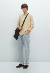 Light beige sweater, light blue jeans, brown suede shoes, and a brown bag with a shoulder strap. Simple design, textured materials.