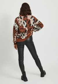 Knitted sweater with a leopard print in brown, orange, and cream; oversized fit. Paired with black leather pants and ankle boots.