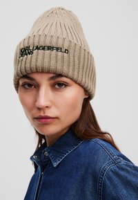 Beige bordázott kötött sapka hegyes tetejével. Elöl hímzett fekete "KARL LAGERFELD JEANS" felirat található.