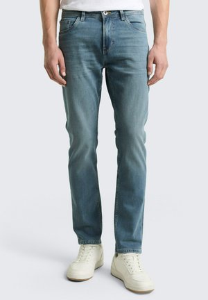 Hellblaue Skinny-Jeans aus Denim mit fünf Taschen, sichtbaren Nähten und Reißverschluss. Kombiniert mit weißen Sneakers.