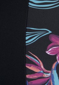 Tissu noir avec un motif floral présentant des accents roses et bleus, avec des textures lisses et une couture reliant deux éléments de design.