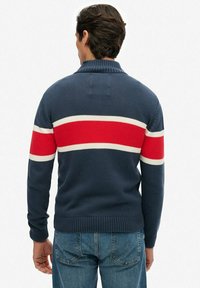 Suéter de punto azul marino con cuello alto, con rayas horizontales rojas y blancas en las mangas. Puños y dobladillo acanalados.