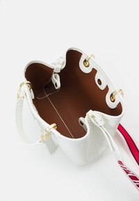 Biała skórzana torba tote z brązowym wnętrzem, złotymi akcentami i odczepianym paskiem na ramię w czerwono-różowe paski, widziana z góry.