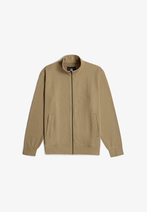 Chaqueta beige con cremallera, cuello alto, mangas largas, dos bolsillos laterales y una textura suave y lisa. Logotipo minimalista en el pecho.