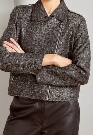 Giacca grigia testurizzata con un design corto e chiusura a zip, dotata di colletto e accessori in argento. Abbinata a pantaloni in pelle scuri.