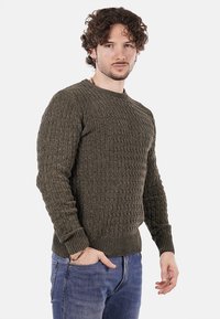 Suéter texturizado en verde oliva con un patrón de canalé, cuello redondo y mangas largas, combinado con jeans azules.