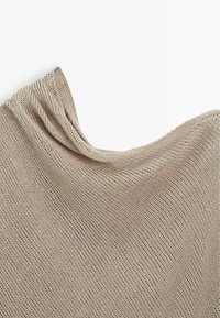 Jasnobeżowa dzianina o luźnym, otwartym splocie i widocznej teksturze, ułożona na białym tle.