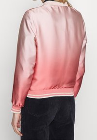 Giacca bomber in satin rosa chiaro, con polsini e orlo a coste e strisce argentate. Texture liscia, design casual.