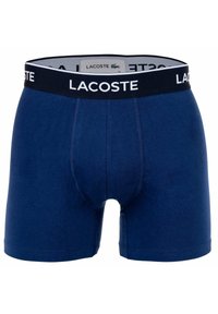 Granatowe bawełniane bokserki z czarnym elastycznym pasem, na którym znajduje się białe logo "LACOSTE". Zawierają otwarcie z przodu i przeszycia.