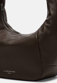 Brązowa skórzana torebka o gładkiej fakturze, zaokrąglonym kształcie i zamknięciu na zamek. Posiada subtelne srebrne logo.