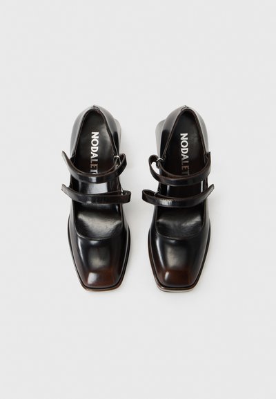 Chaussures en cuir noir avec un bout carré, deux sangles ajustables et un talon bas. Fini lisse avec un subtil dégradé de couleur.