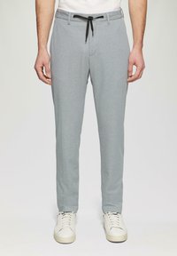 Helle graue Hose mit strukturierten Oberflächen, Kordelzugbund und Seitentaschen, kombiniert mit weißen Sneakers.