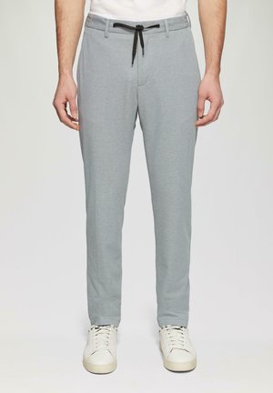 Helle graue Hose mit strukturierten Oberflächen, Kordelzugbund und Seitentaschen, kombiniert mit weißen Sneakers.