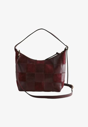 Dunkelrote Patchwork-Schultertasche mit kurzen und langen Trägern und einem oberen Reißverschluss vor weißem Hintergrund.