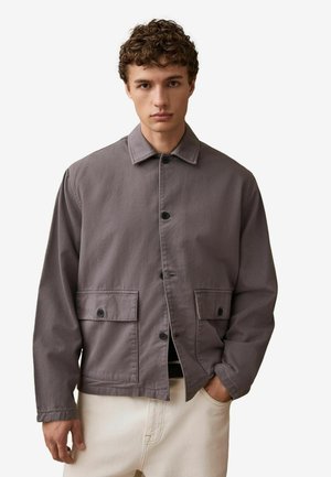 Pilkas medvilninis švarkas su sagų užsegimu, dviem priekinėm kišenėm ir klasikiniu apykakle. Audinys yra lygios tekstūros ir laisvo kirpimo.